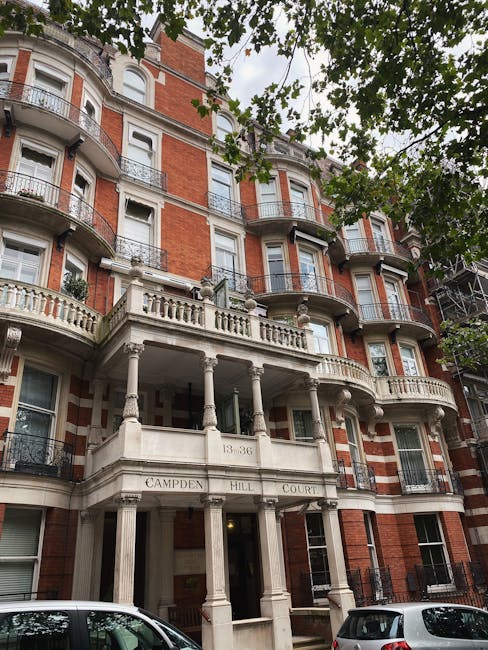A row of elegant, multi-storey Georgian townhouses with light-colored brick facades and white-framed sash windows, located along a busy urban street on a clear day with blue sky and scattered clouds. 